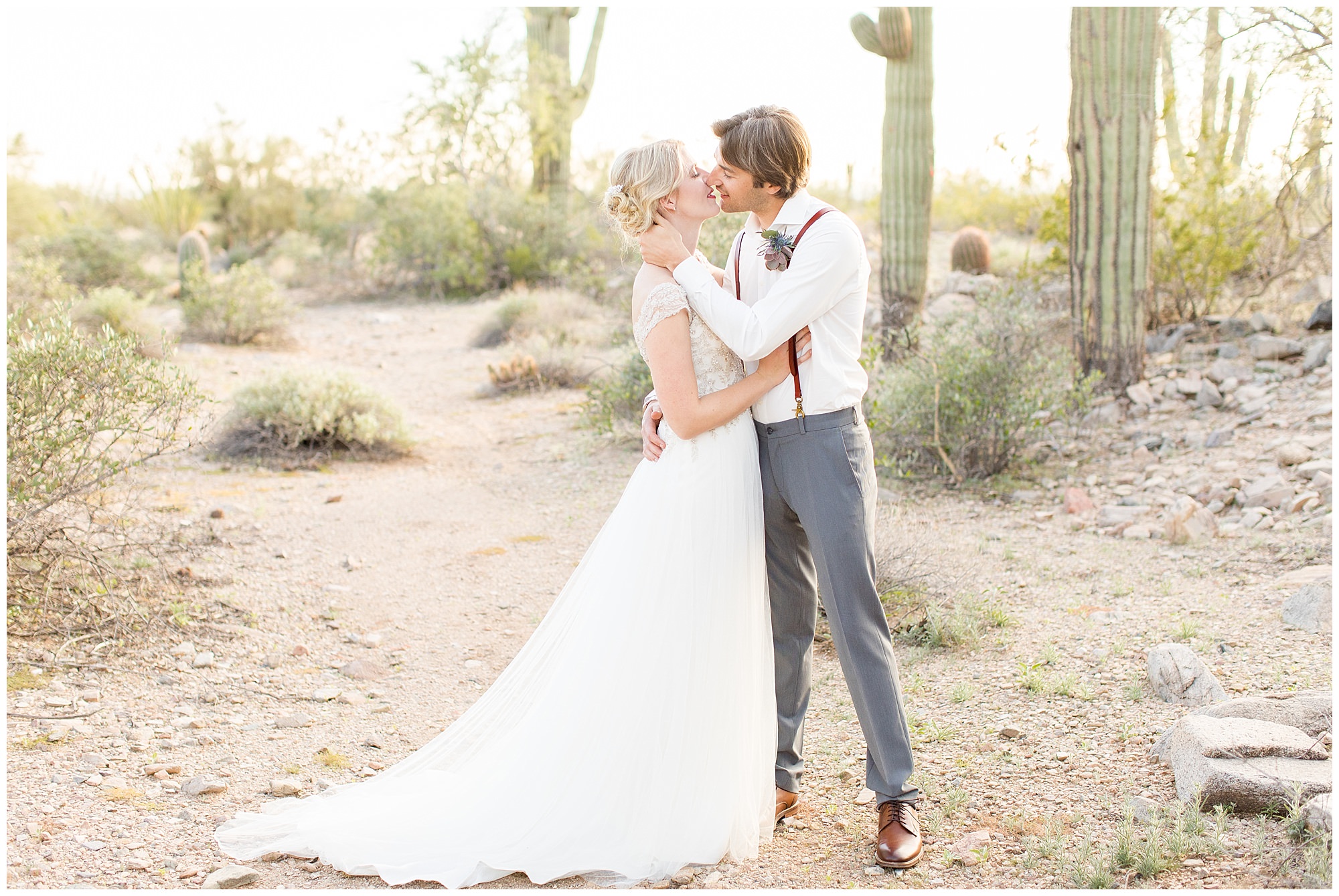groom gently holding bride while kissing in the desert