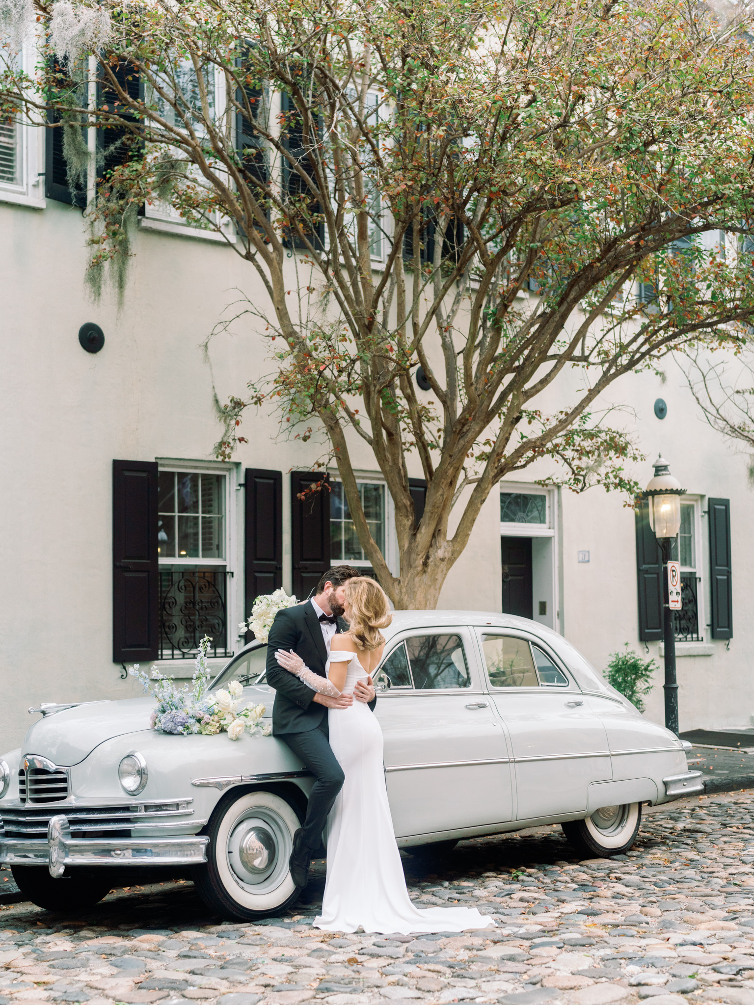 bride and groom kiss next o vintage car on historic cobblestone streets in downtown charleston